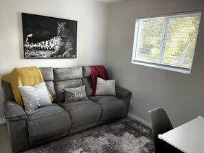 A grey sofa with a throw blanket, a cushion with 'love' written on it, and a black and white leopard print artwork on the wall.