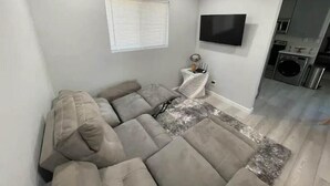 Een moderne woonkamer met een modulaire bank, een flatscreen televisie aan de muur en een wasruimte met wasmachine en droger.