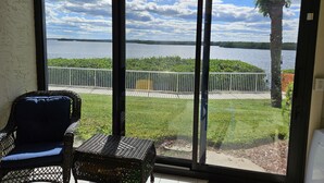 Une pièce dotée d’une grande fenêtre donnant sur un lac, d’un fauteuil en osier et d’une petite table.