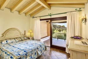 Ein Schlafzimmer mit Bett, Nachttisch, Lampe, Kommode und einem Balkon mit Ausblick ins Freie.