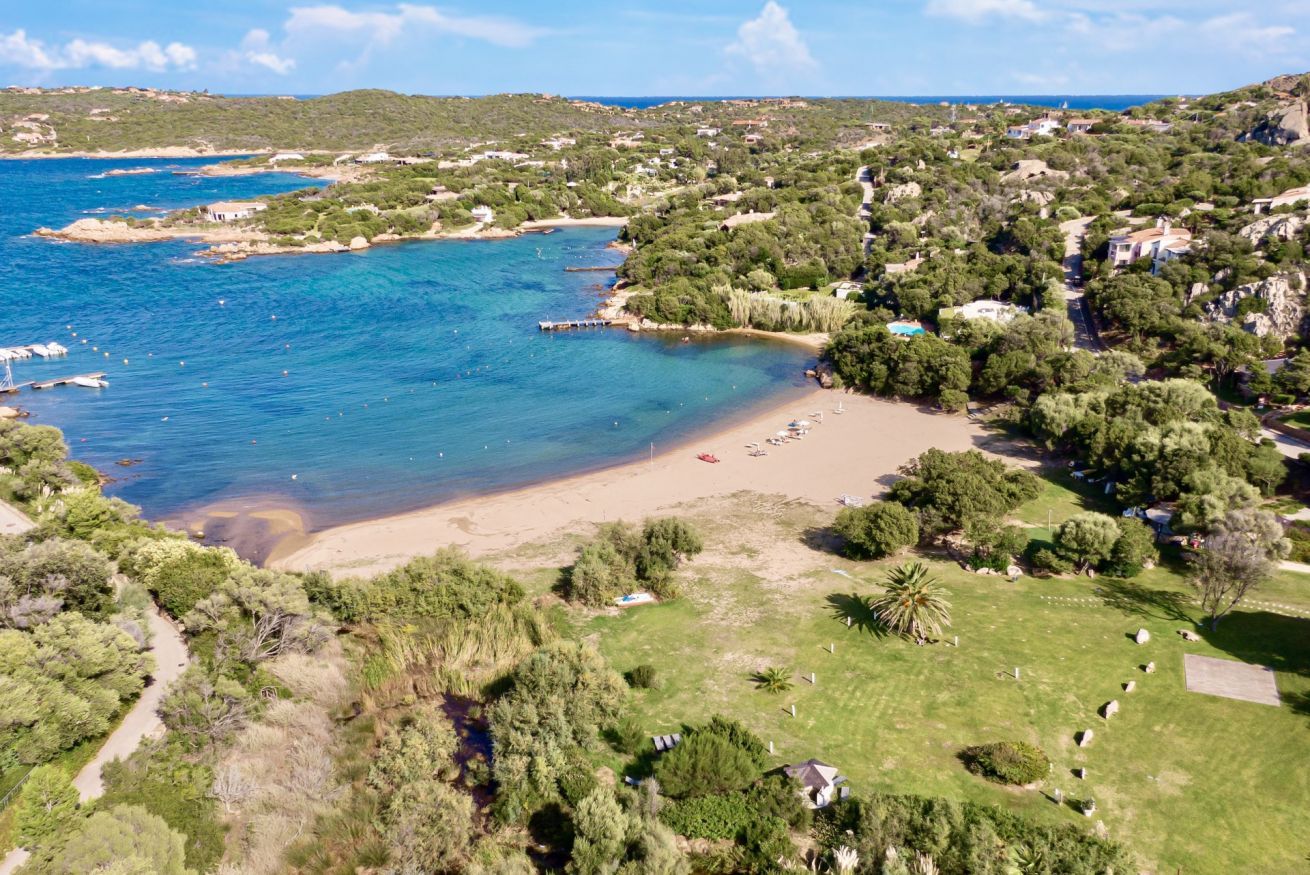 Luftaufnahme einer Küstenlandschaft mit Strand, klarem blauen Wasser und umgebender Bepflanzung.