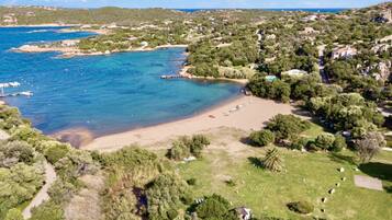 Luftaufnahme einer Küstenlandschaft mit Strand, klarem blauen Wasser und umgebender Bepflanzung.