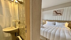 A hotel room with a bathroom, a bed with white bedding, and a wall-mounted light fixture. - ROLANDO BEDS Bariloche (San Carlos de Bariloche)
