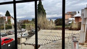 A view through a window with a tiled roof, a staircase, and a distant landscape including trees and buildings. - ROLANDO BEDS Bariloche (San Carlos de Bariloche)
