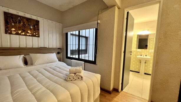 A bedroom with a large bed, a window, a radiator, and a bathroom visible through an open door. - ROLANDO BEDS Bariloche (San Carlos de Bariloche)