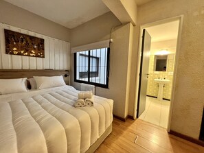 A bedroom with a large bed, a window, a radiator, and a bathroom visible through an open door. - ROLANDO BEDS Bariloche (San Carlos de Bariloche)