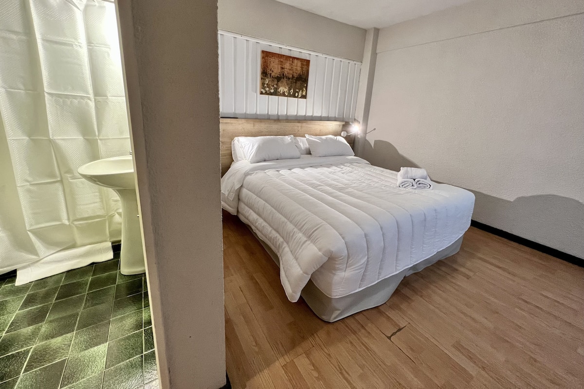 A neatly arranged hotel room with a bed, a bedside table, a wall-mounted artwork, and a shower curtain.