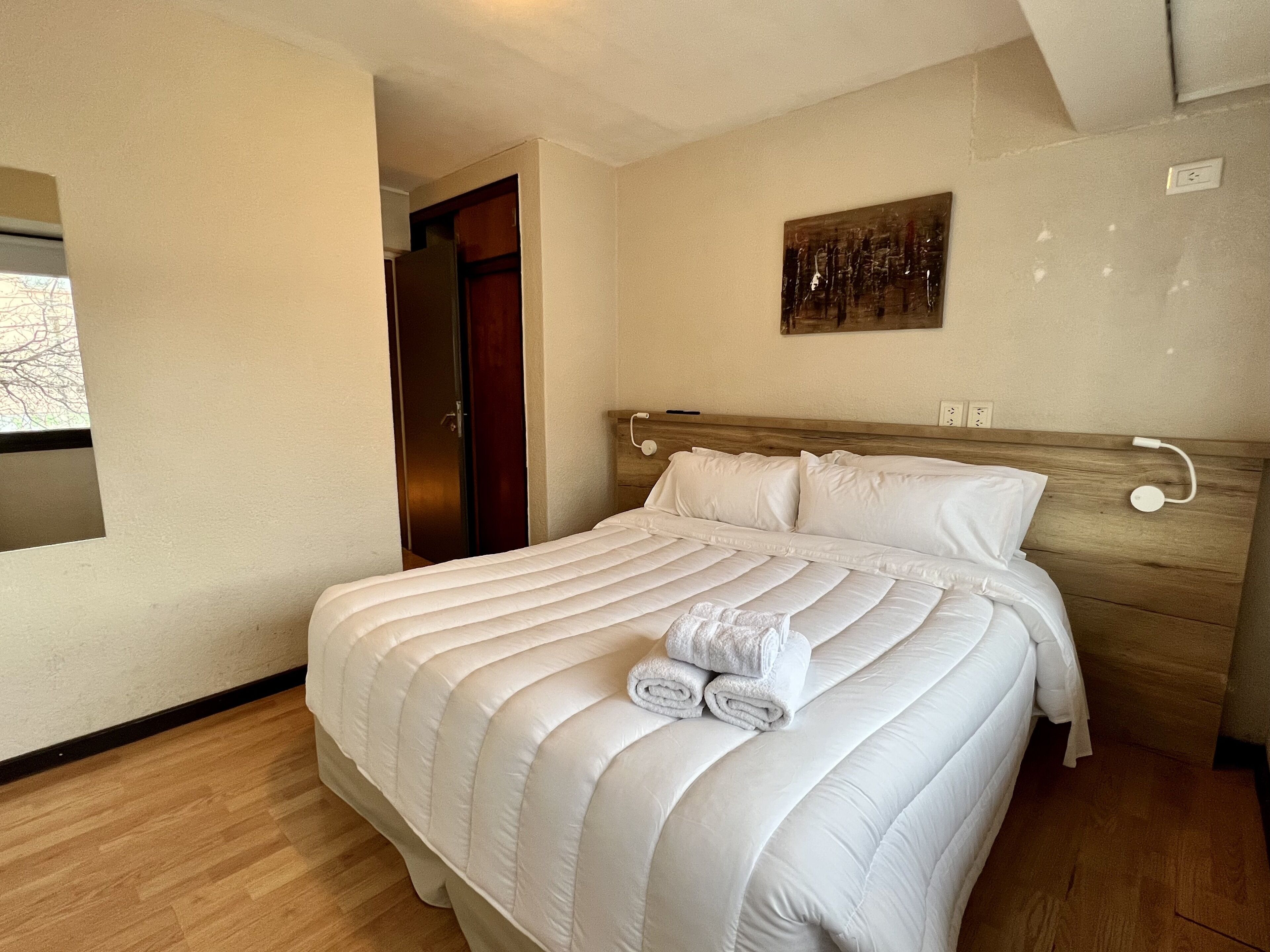 Een net opgemaakt bed met een houten hoofdbord, een schilderij aan de muur en een houten vloer.