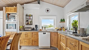 A modern kitchen with wooden cabinets, a dishwasher, and a window providing a view of the outdoors. - Cozy home in Otterup with WiFi (Otterup)