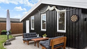 A patio with two grey cushioned chairs and a wooden table, a dartboard, and a white umbrella. - Cozy home in Otterup with WiFi (Otterup)