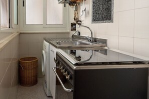 Une cuisine compacte dotée d’un évier en acier inoxydable, d’un four encastré et d’un lave-linge.