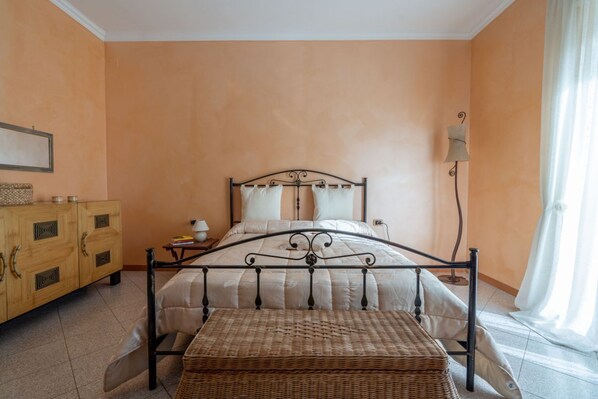 Une chambre à coucher comprenant un lit, une table de chevet, une lampe, une commode et une fenêtre avec des rideaux.