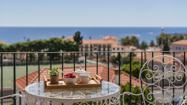 A balcony with a table set for tea, a potted plant, and strawberries. - Vacations in Funchal, sea view - Casa Strelitzia II (Funchal)