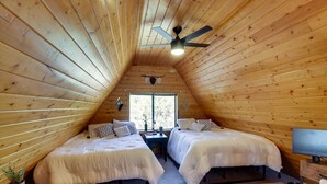 A cozy attic bedroom with two beds, a ceiling fan, a TV, and a window. - Decks + Fire Pit: Rustic-Modern Overgaard Cabin! (Overgaard)