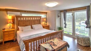 Een slaapkamer met een houten bed, nachtlampjes, een raam met zonwering en uitzicht op de omgeving.