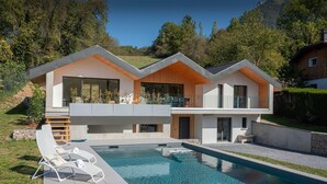 Et moderne hus med to etager, en swimmingpool, store vinduer og en træterrasse.