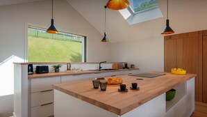 Et moderne køkken med en træø med hængende lamper og udsigt over et grønt landskab gennem et ovenlys.