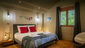 Ein Schlafzimmer mit Holzboden, einem Bett mit weißer und roter Bettwäsche, einem Nachttisch mit Lampe und einem Fenster mit Blick auf Grünflächen.