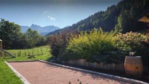 Ein Kiesplatz mit einem hölzernen Fass und einem Picknicktisch, umgeben von üppiger Vegetation und einer Bergkulisse.