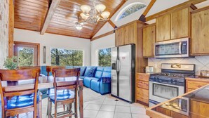 Un'ampia cucina con pensili in legno, un frigorifero, un piano cottura e un'area pranzo con un divano blu e sedie in legno.