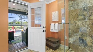 Une salle de bain avec une douche en verre, une porte blanche et une vue sur un espace extérieur agrémenté d’une statue de flamant rose.