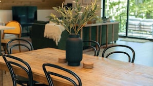 A dining area with a wooden table, black chairs, a vase with greenery, and a hanging light fixture. - Modern Aframe with River Views, Sauna, Hot Tub (Fennville)