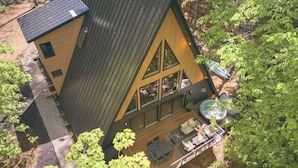 A cabin with a sloped roof, large windows, and a deck with outdoor furniture. - Modern Aframe with River Views, Sauna, Hot Tub (Fennville)