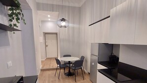 Cozinha moderna com armários brancos, bancada preta e área de jantar com mesa e cadeiras redondas.