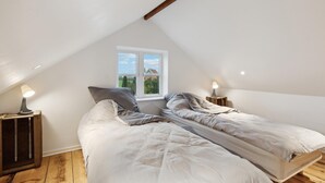 Slaapkamer met schuine kap, twee nachtkastjes met lampen, een raam met uitzicht op groen, en een bed met wit beddengoed.