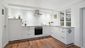 Een moderne keuken met witte kasten, een inbouwoven en een raam dat voor natuurlijk licht zorgt.