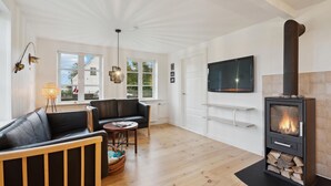 Een moderne woonkamer met een zwarte leren bank, een houten salontafel, een open haard en een aan de muur bevestigde televisie.