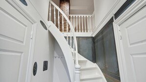 Een witte trap met houten leuning, leidend naar een plateau met een stenen muur en een deur met decoratief paneel.