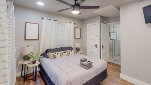 Une chambre à coucher avec un lit, un ventilateur de plafond, une table de chevet avec une lampe et une plante en pot.