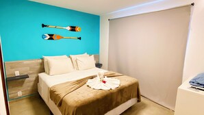 A hotel room with a bed, a blue accent wall, and a window with a blind.