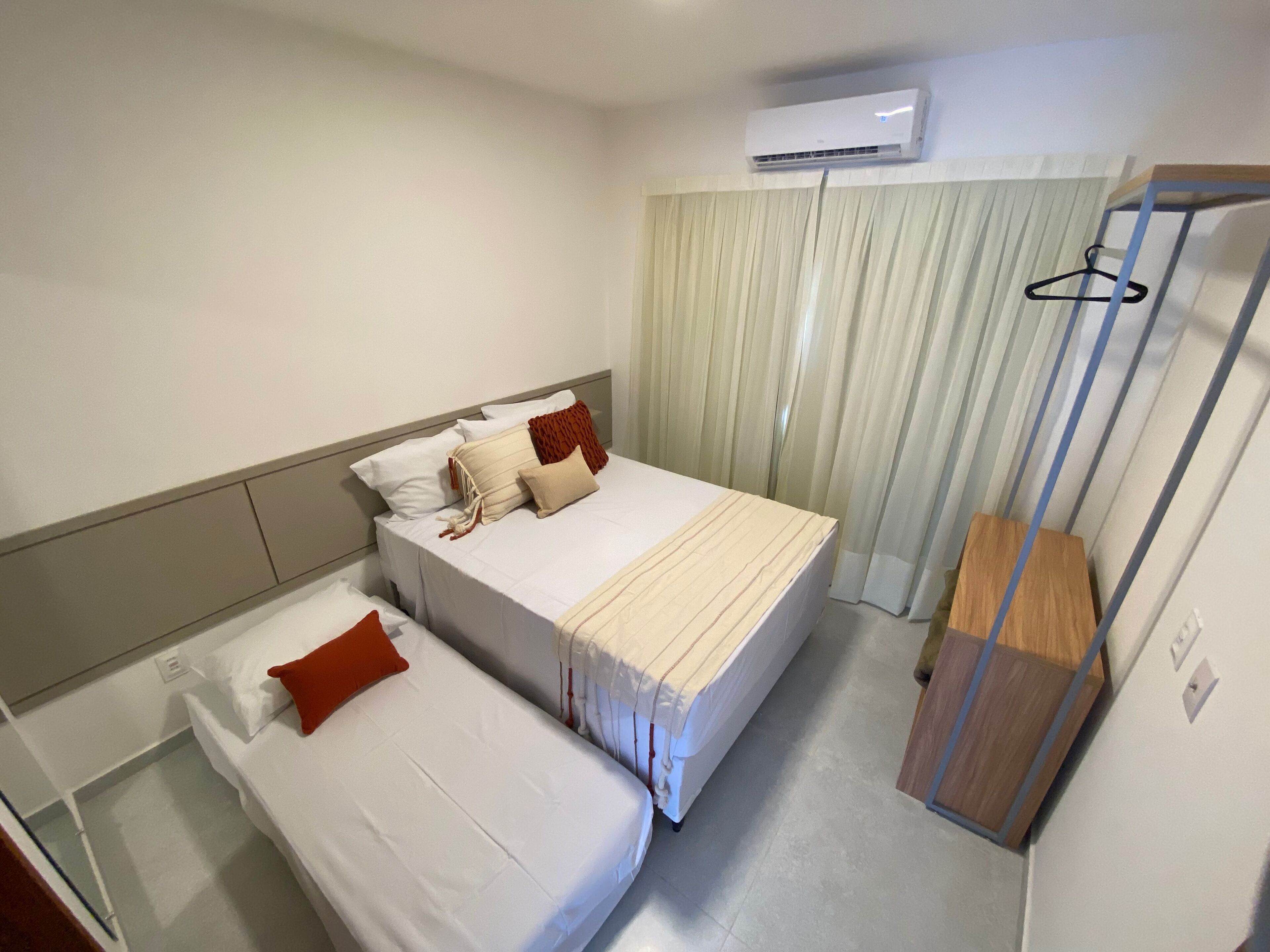 A hotel room with two single beds, a wooden nightstand, an air conditioning unit, and a curtain.