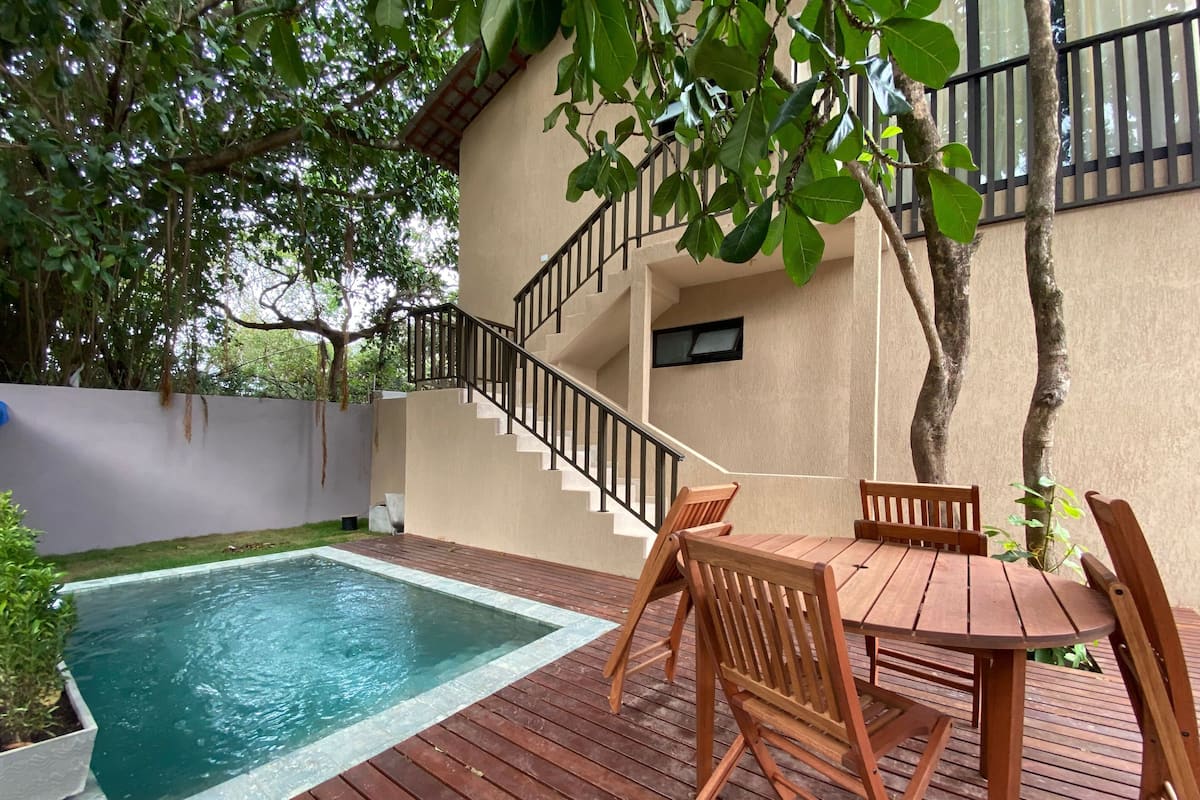 Ein Poolbereich mit Holzterrasse, einem Tisch mit Stühlen und einer Treppe zu einer erhöhten Ebene.