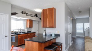 A kitchen with wooden cabinets, a black countertop, and two stools. There is a sign on the wall that says "Kitchen Together." - Spacious 4BR - King Bed - Near I-70 (Dayton)