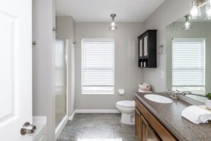 A bathroom with a shower, toilet, sink, and vanity. - Spacious 4BR - King Bed - Near I-70 (Dayton)