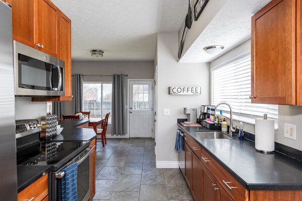 A kitchen with wooden cabinets, a stainless steel microwave, a stove, and a sink. - Spacious 4BR - King Bed - Near I-70 (Dayton)