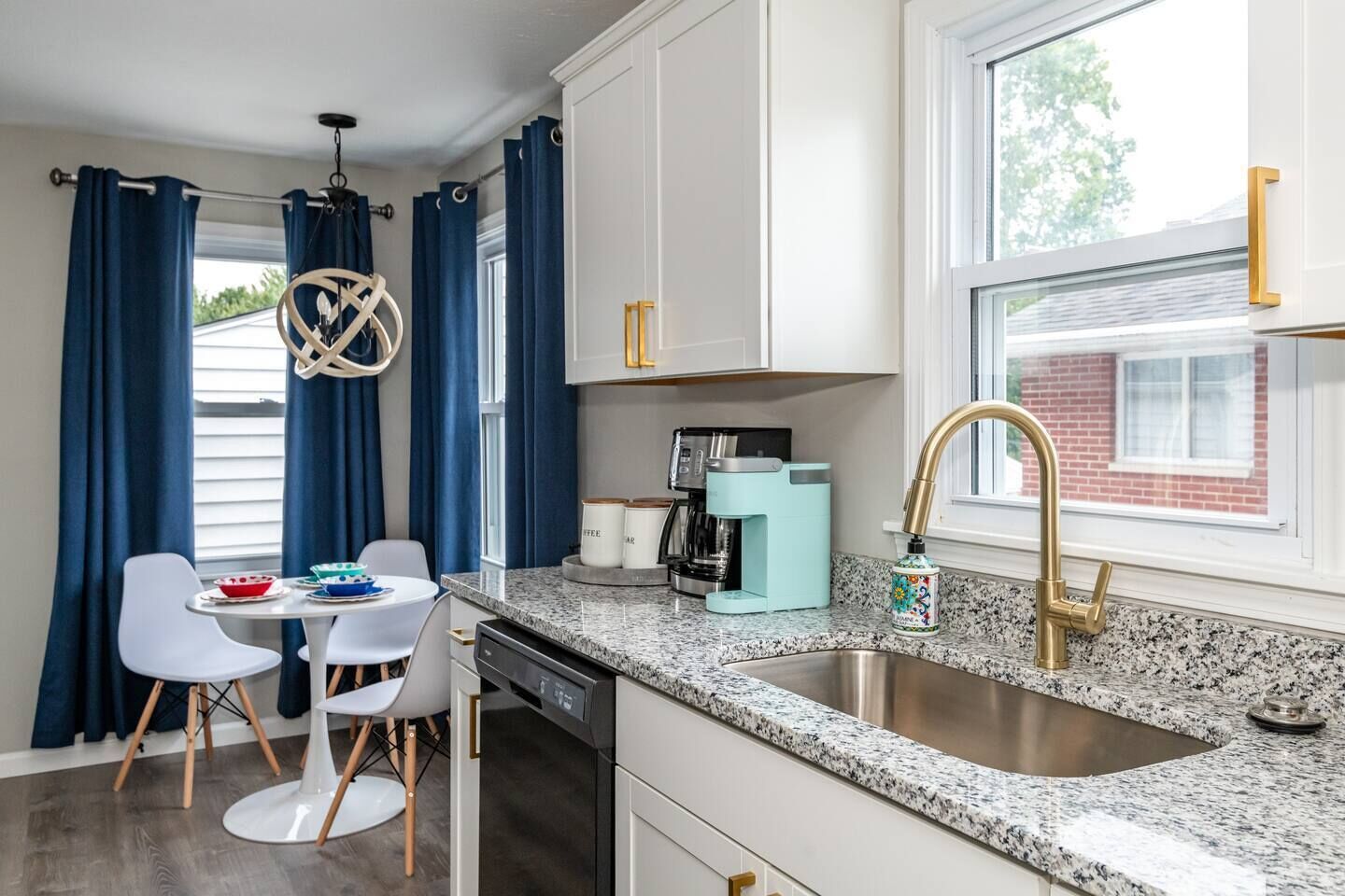 A modern kitchen with white cabinets, a granite countertop, a stainless steel sink, and a coffee maker.