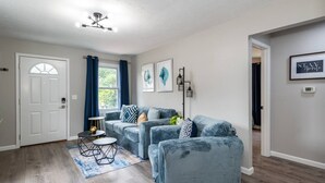 A living room with a grey sofa set, a small round table, and a blue rug. There is a white door with a window and blue curtains. - Remodeled-Pet friendly-5 min to WPAFB and Downtown (Dayton)