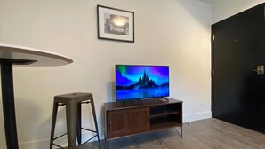 Una sala de estar moderna con un televisor de pantalla plana sobre un mueble de madera, un taburete de bar y un cuadro enmarcado en la pared.