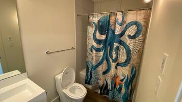 A bathroom with a white toilet, a shower curtain with a sea creature design, and a wooden floor.
