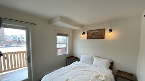 Un dormitorio con cama, ventana, puerta y balcón.