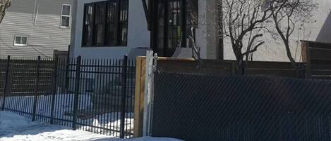 A two-story building with a white facade, black-framed windows, and a black metal fence in front.