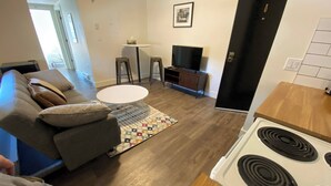 Una sala de estar con sofá, mesa de centro, televisor y una cocina con estufa.