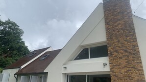 Une maison moderne avec un toit en pente, une cheminée en briques et une grande porte vitrée.