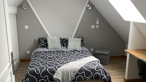 Une chambre avec un plafond en pente, un lit recouvert d’une literie à motifs, un tapis gris, un bureau et une fenêtre laissant entrer la lumière naturelle.
