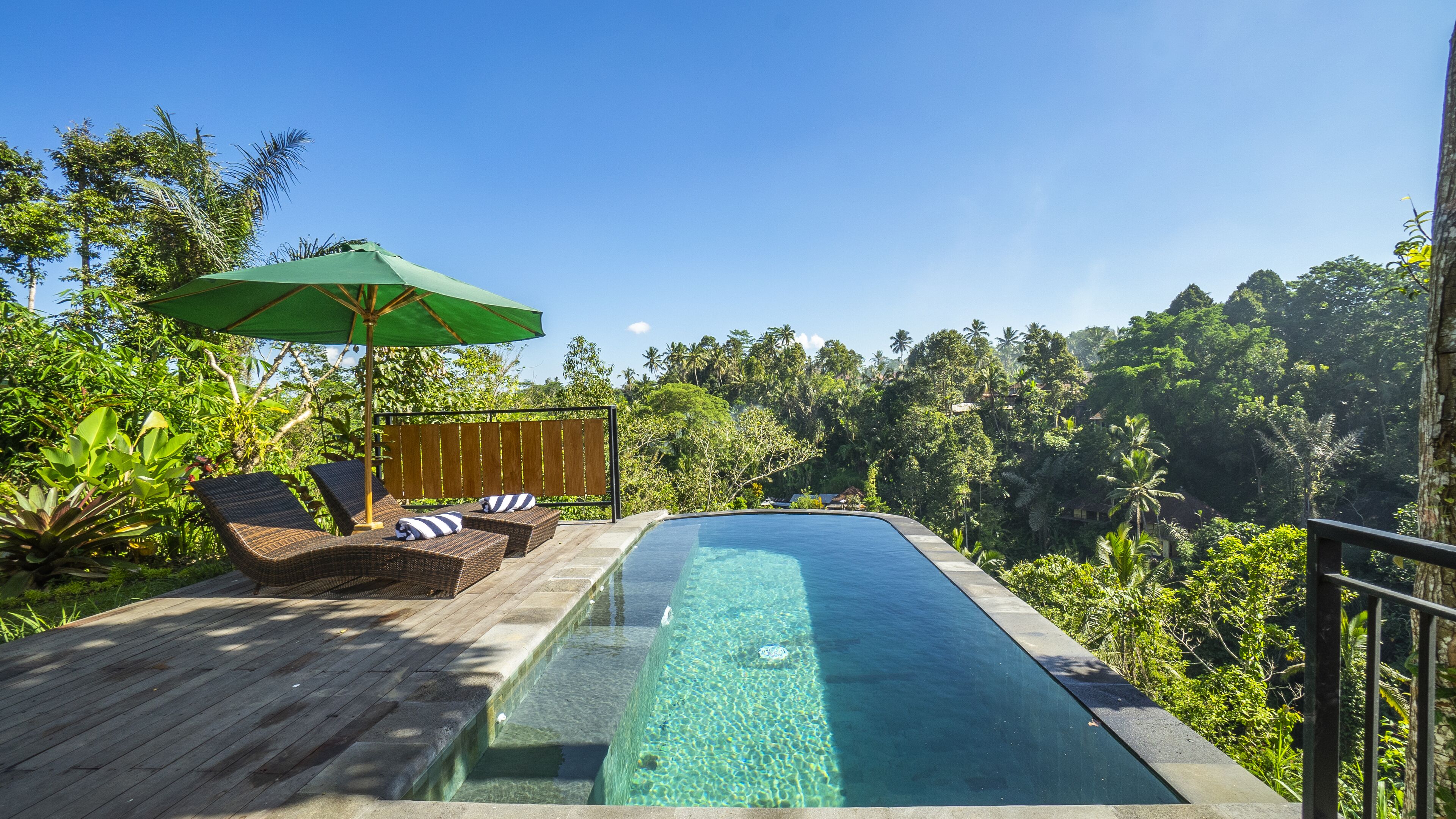 An infinity pool with a wooden deck, lounge chairs, and a green umbrella.