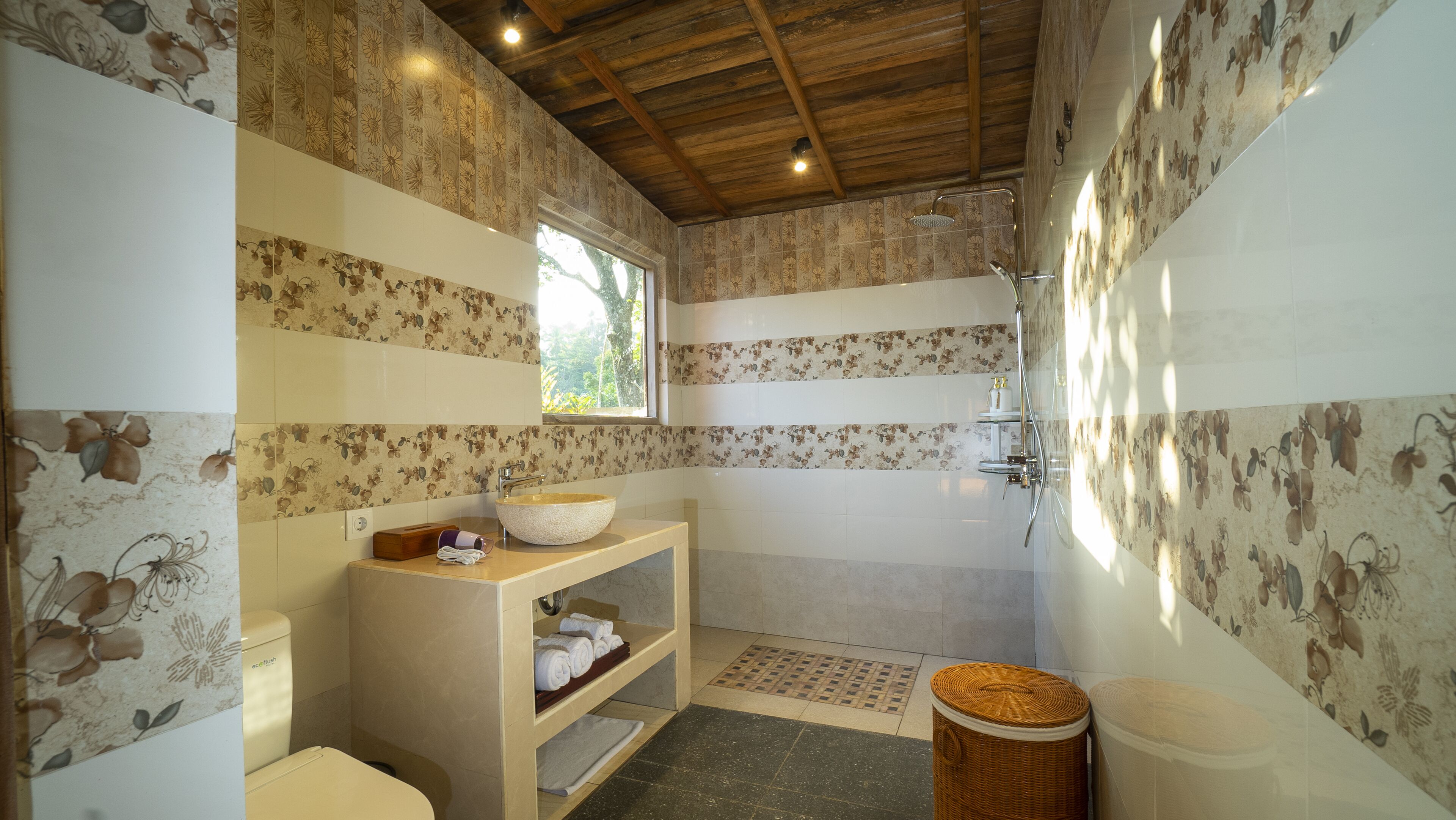 A bathroom with a wooden ceiling, a sink, a shower, and a shelf with towels.